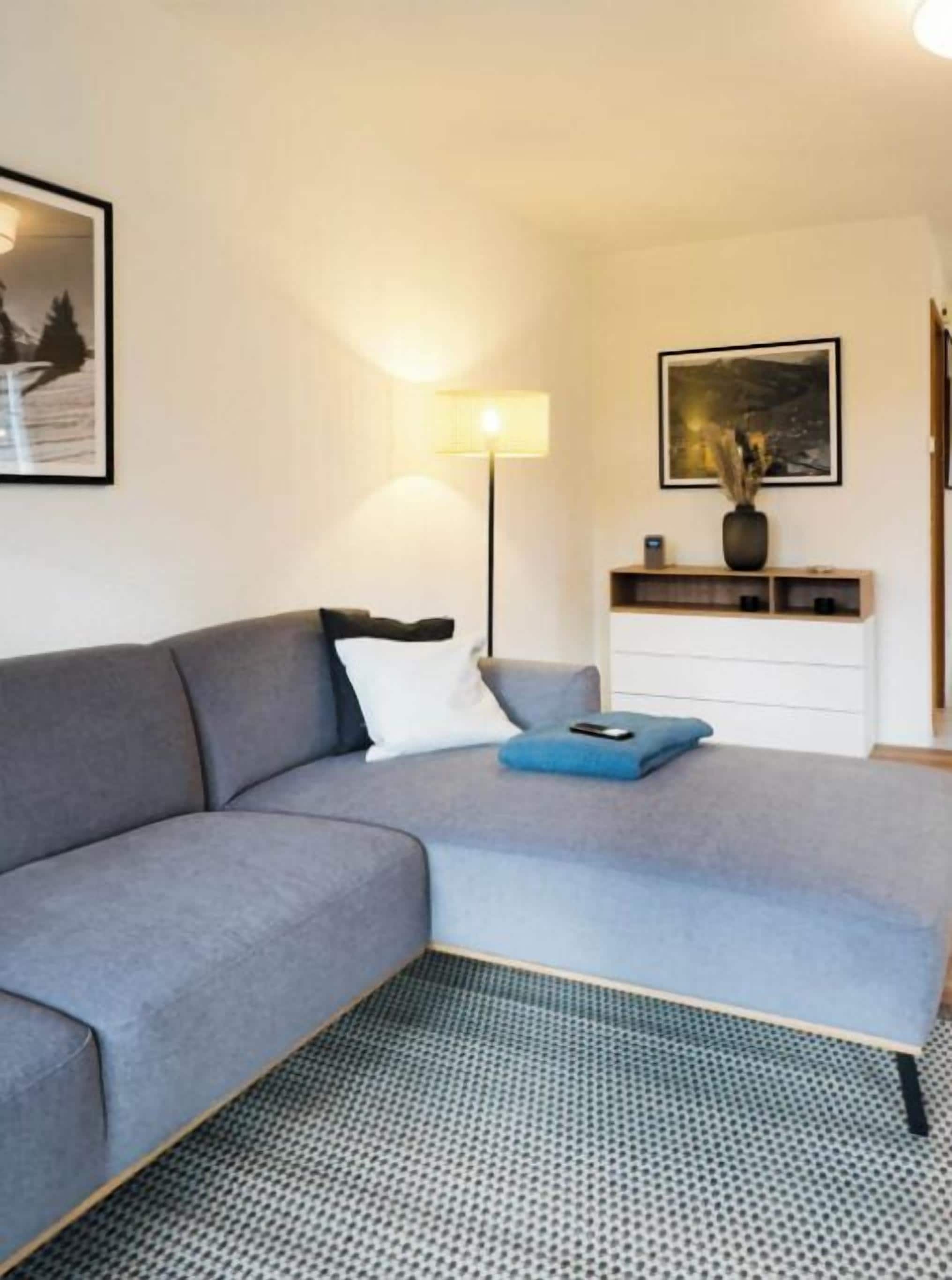 Un salón moderno con un sofá gris, una mesita auxiliar, una lámpara y un cuadro en la pared.