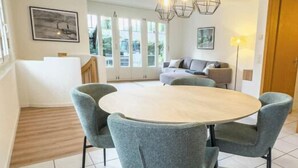 Een eetruimte met een ronde tafel en vier stoelen, een trap naar een hoger niveau, en een bank op de achtergrond.