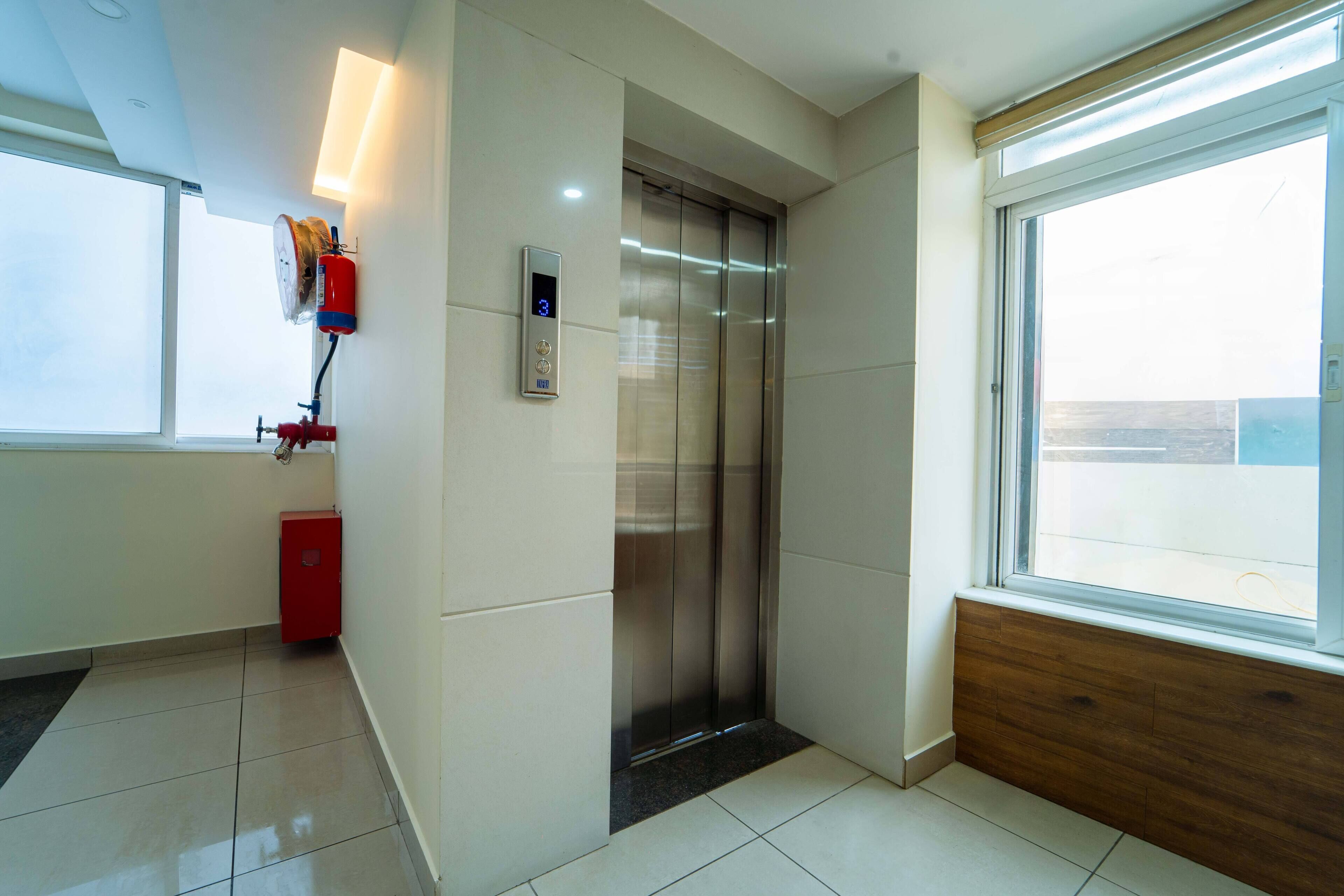 Een moderne lift met een digitaal display, een rode brandblusser en een raam met uitzicht.