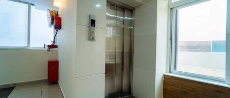 A modern elevator with a digital display, a red fire extinguisher, and a window with a view of the outside.