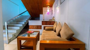 A modern living room with a wooden ceiling, a glass staircase, a sofa with cushions, and a decorative wall piece. - Treebo Sree Varshavilas Regency, 500 Mtrs From Guruvayoor Temple (Chavakkad)