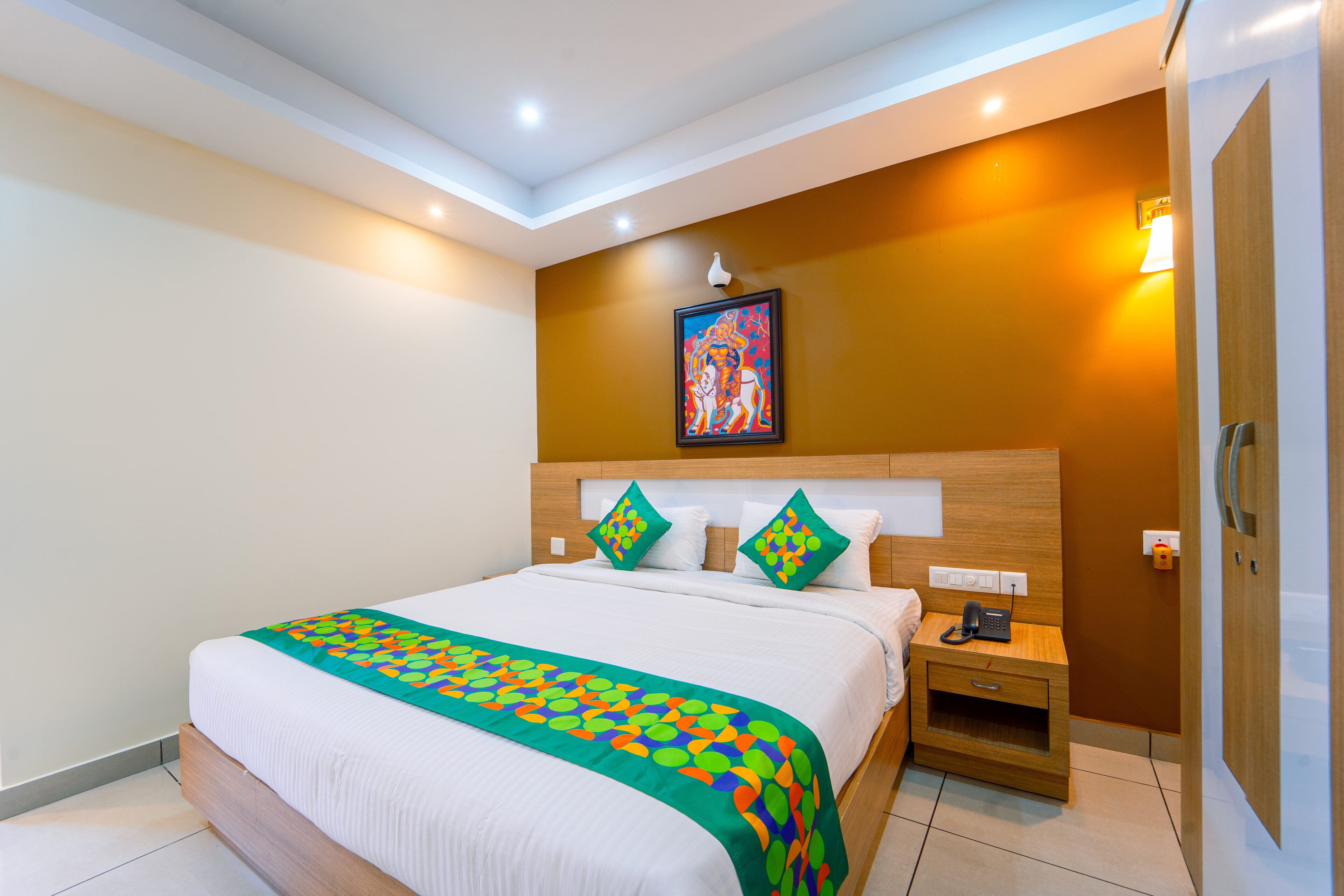 Un cuarto de hotel con una cama grande, una mesita de noche con lámpara y un cuadro en la pared.