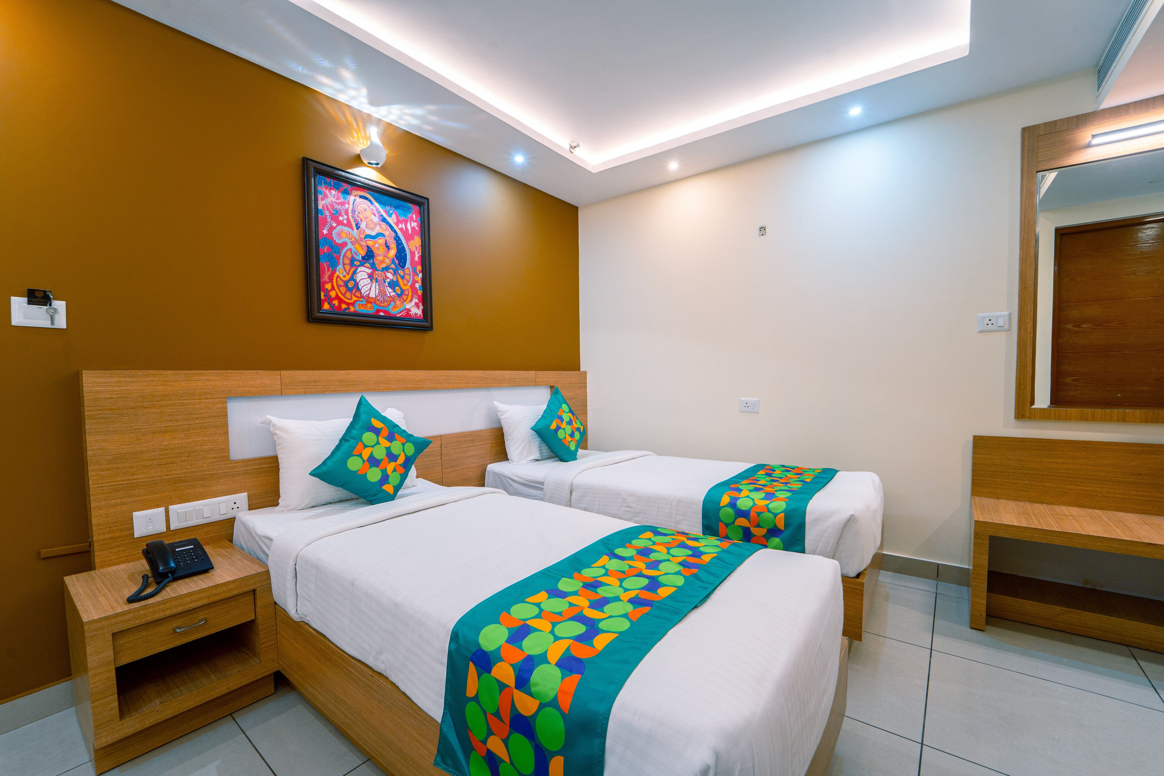 A hotel room with two beds, a wooden headboard, a nightstand with a phone, and a colorful artwork on the wall.