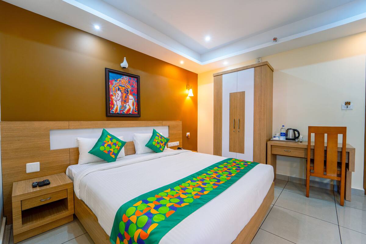 A hotel room with a large bed, a desk, a chair, a nightstand, a painting on the wall, and a wardrobe.