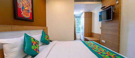 A hotel room with a neatly made bed, a television mounted on the wall, and a framed artwork above the bed.