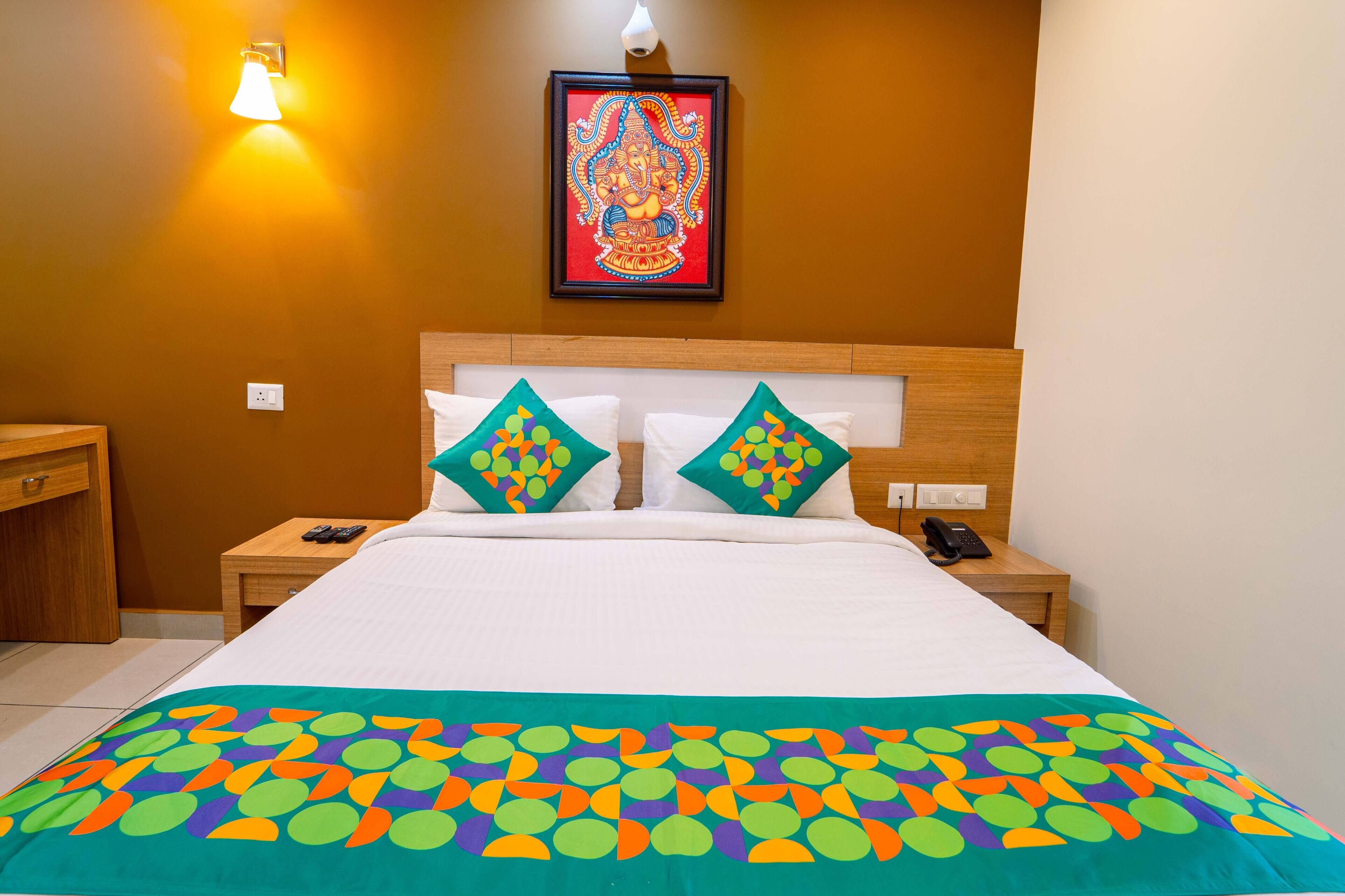 A hotel room with a bed, two pillows, a nightstand, a wall-mounted light, and a framed picture.