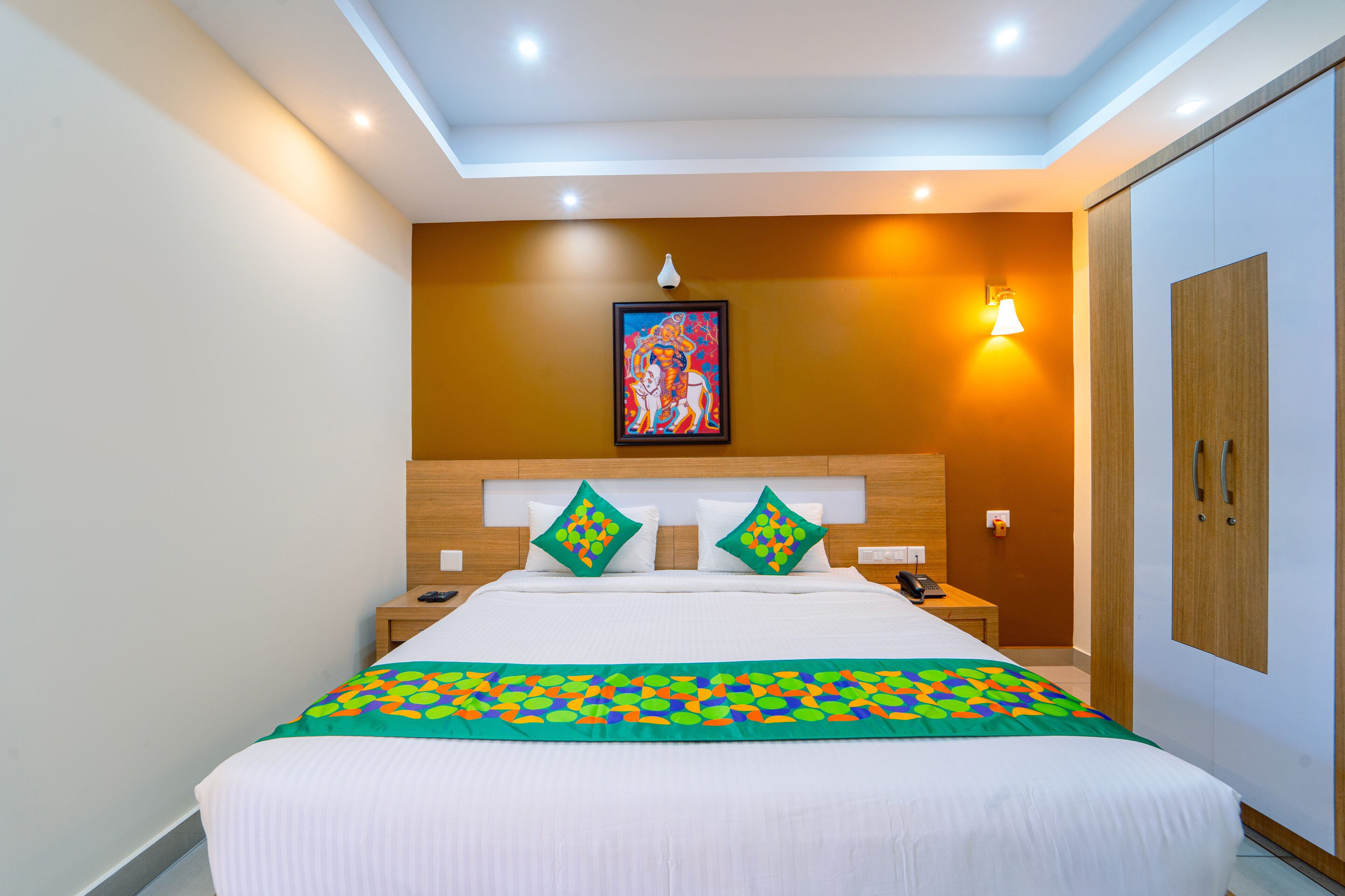 A hotel room with a large bed, a nightstand, a bedside table, a wall-mounted lamp, and a wardrobe.