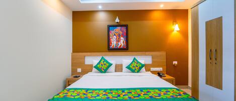 A hotel room with a large bed, a nightstand, a bedside table, a wall-mounted lamp, and a wardrobe.