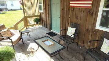 Une véranda en bois avec une table et des chaises, une porte verte et un drapeau américain.