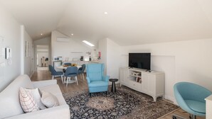 A modern living room with a sofa, a blue armchair, a TV, and a dining area with chairs and a table. - The Fort of Old Town 3 by Our Madeira (Funchal)