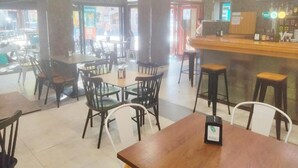 A restaurant with multiple tables and chairs, a bar area with stools, and a view of the street outside. - HOTEL LAUAXETA MUNGUIA (Mungia)