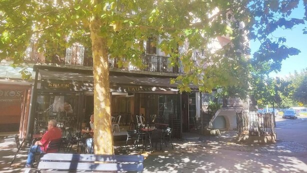 An outdoor seating area with tables and chairs under a tree, a building with 'KELER' signage, and a parked car in the background. - HOTEL LAUAXETA MUNGUIA (Mungia)