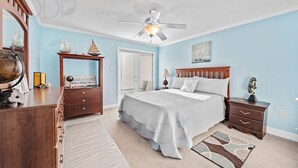 Un dormitorio con cama, mesitas de noche, cómoda, ventilador de techo y una puerta con ventana.