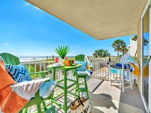 Ein Balkon mit grünen Stühlen, einem kleinen Tisch und Blick aufs Meer.