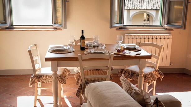 A dining area with a table set for four, including plates, glasses, and a bottle of wine. There are two chairs with checkered cloths, and a radiator is visible in the background. - RIDOLFO HOUSE - Apartment in San Miniato (San Miniato)