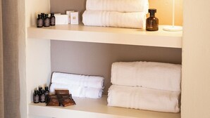 Um banheiro com prateleiras contendo toalhas, velas e produtos de higiene pessoal.