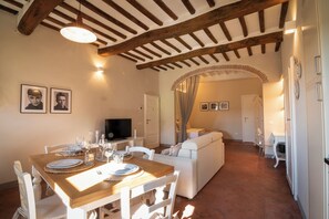 A dining area with a wooden table set for four, a television on a stand, and a white sofa in the background. - RIDOLFO HAUS - Apartment in San Miniato (San Miniato)