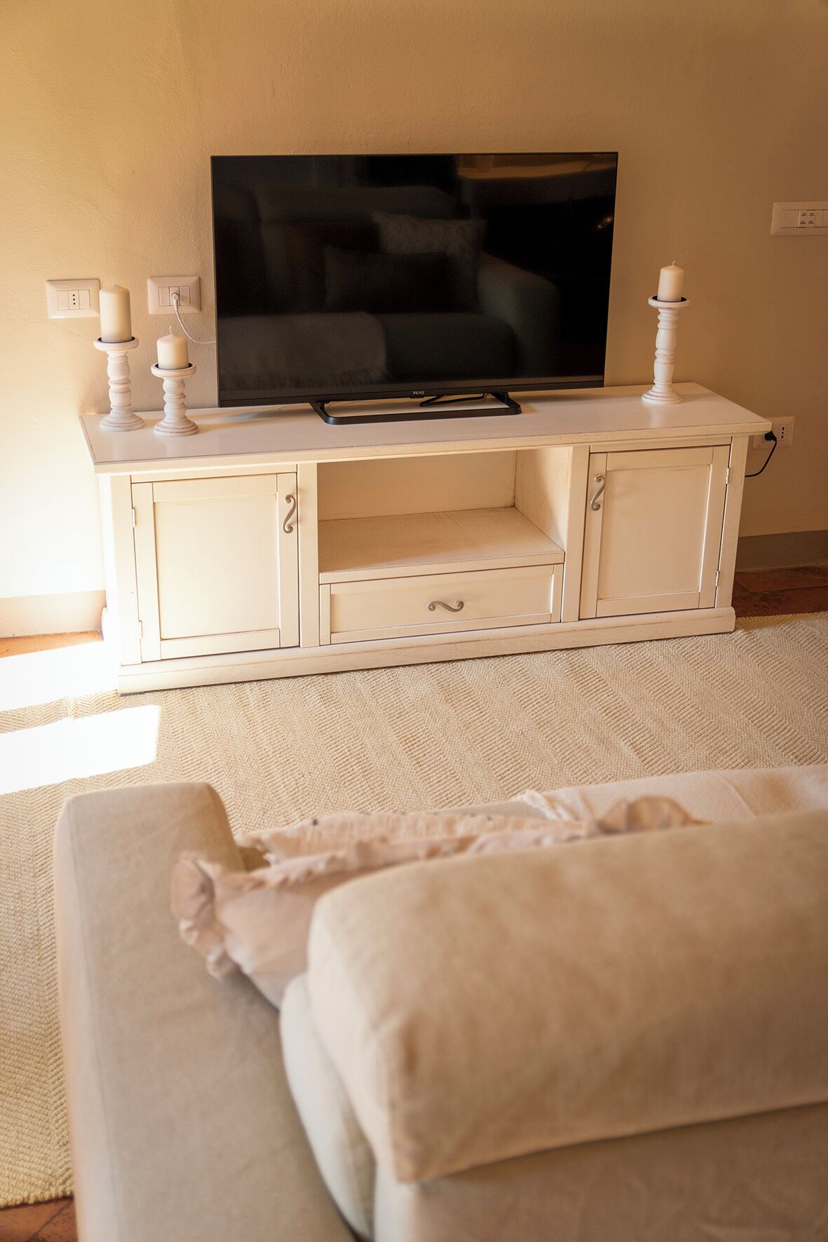 A living room with a flat-screen TV on a white cabinet, a sofa, and a small table with candles.