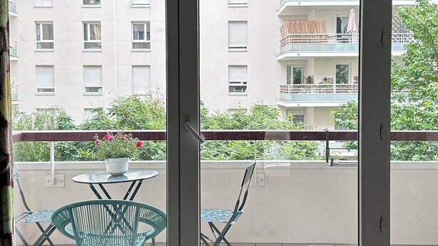 Ein Balkon mit Tisch und Stühlen, einem Blumentopf und Blick auf ein mehrstöckiges Gebäude.