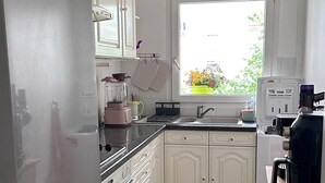 Eine Küche mit weißen Schränken, einem eingebauten Backofen, einer Spüle und einem Fenster mit Blick auf Grünflächen.