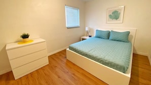 Un dormitorio con cama, mesita de noche, cómoda y ventana con persianas.