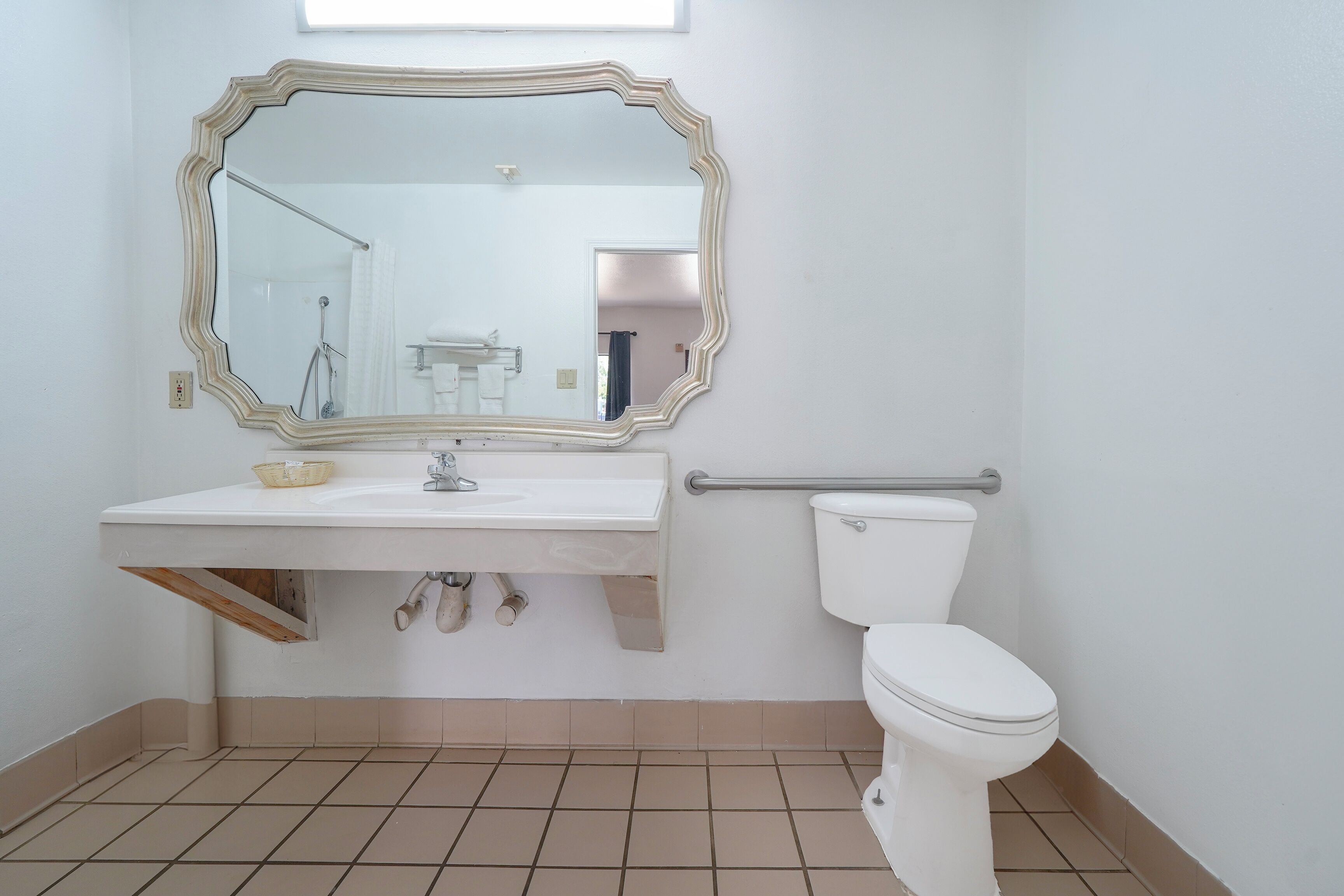A bathroom with a white sink, a mirror with a decorative frame, a toilet, and a grab bar.