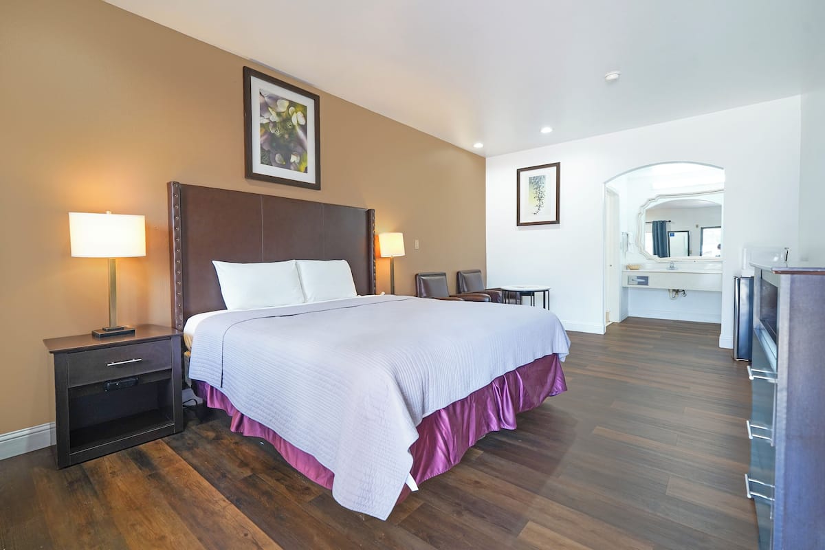 A hotel room with a large bed, two bedside tables with lamps, a small desk, and a mirror.