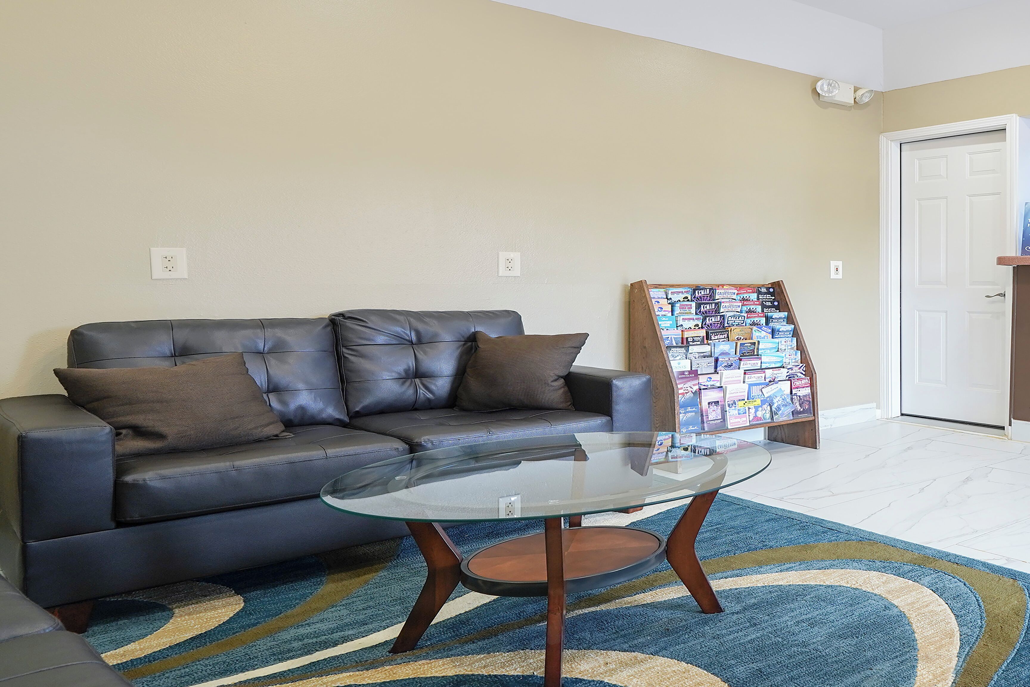A living room with a leather sofa, a glass coffee table, a patterned rug, and a bulletin board with cards.