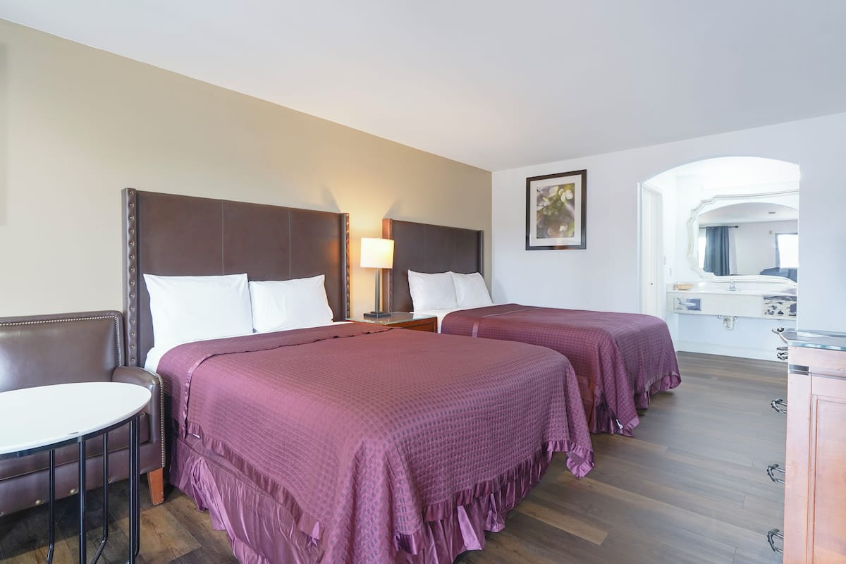 A hotel room with two beds, a small table, and a mirror.