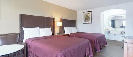A hotel room with two beds, a small table, and a mirror.