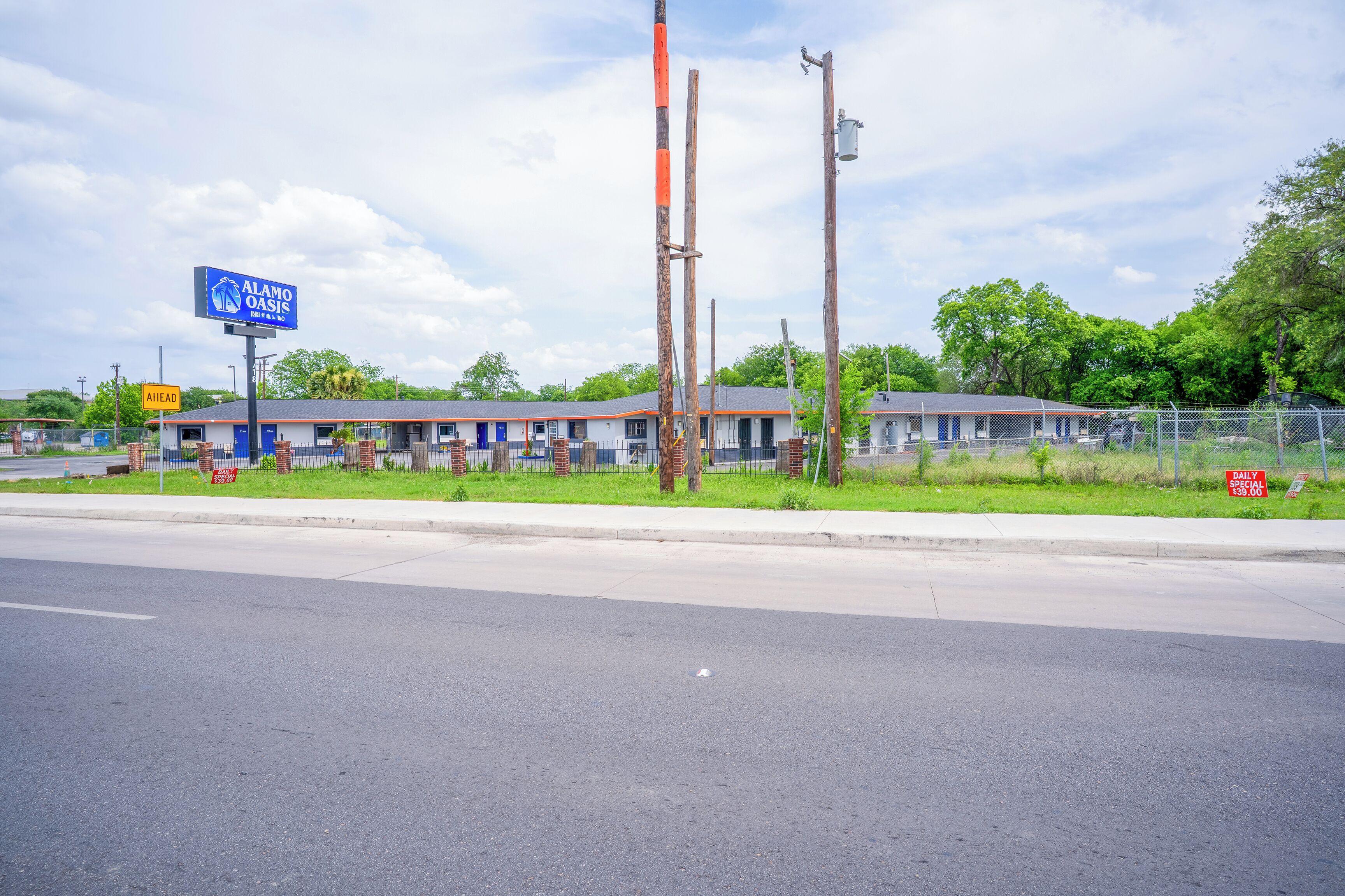 A motel with a blue sign, a fenced parking area, and a road in front.