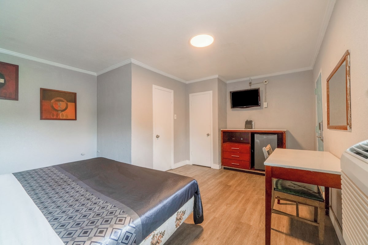 A bedroom with a bed, a desk, a chair, a television, and a mirror.