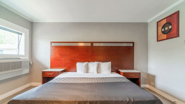 A hotel room with a large bed, wooden headboard, two bedside tables, and a window with curtains. - Alamo Oasis Inn And Suites By Oyo San Antonio (San Antonio)