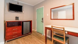 A compact room with a wooden desk, a chair, a television mounted on the wall, and a small refrigerator. - Alamo Oasis Inn And Suites By Oyo San Antonio (San Antonio)