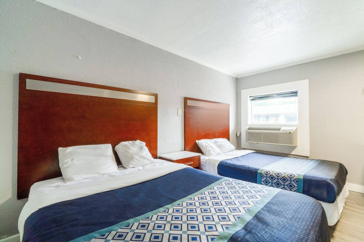 A hotel room with two beds, each with a wooden headboard, white bedding, and a patterned bedspread.