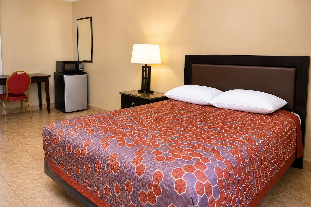 Une chambre d’hôtel équipée d’un lit, d’un bureau, d’une chaise, d’une lampe et d’un petit réfrigérateur.
