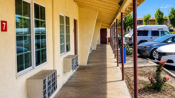A covered outdoor corridor with a concrete walkway, a building with numbered windows, and parked cars. - Sai Park Motel (Lancaster)