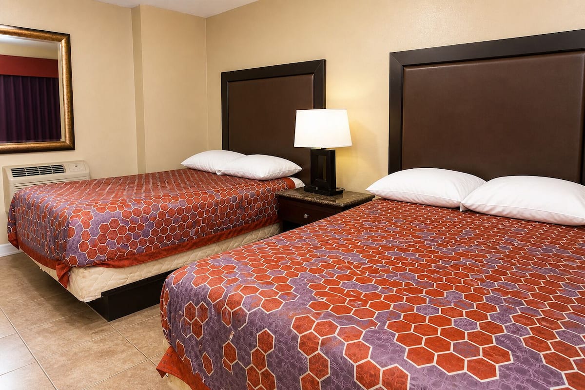 Une chambre d’hôtel avec deux lits, une table de chevet avec une lampe, un miroir et un climatiseur fixé au mur.