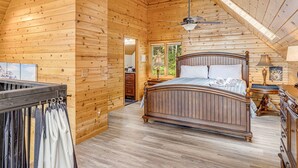 A wooden cabin bedroom with a bed, a ceiling fan, and a view of the outdoors.