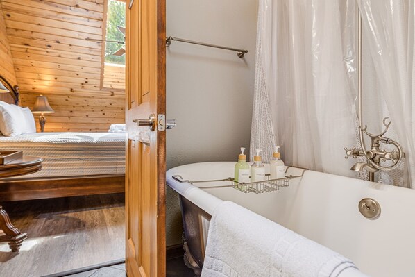 Un dormitorio de cabaña de madera con una cama, un aparador de madera y un baño con bañera, ducha y toallero.