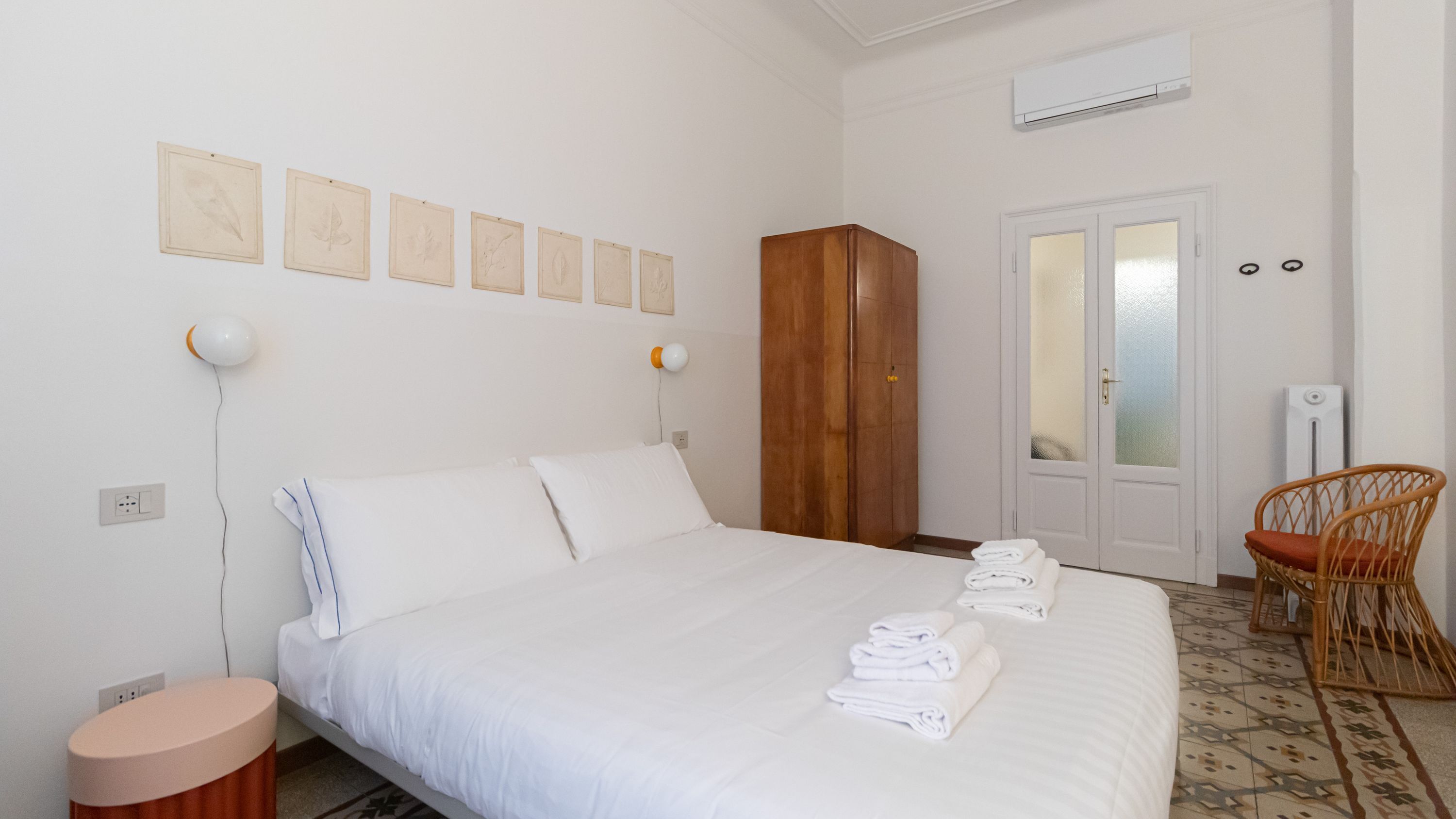 A hotel room with a bed, a wardrobe, a chair, and wall-mounted artwork.