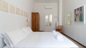 A hotel room with a large bed, a wooden wardrobe, a wicker chair, and a framed artwork on the wall. - Italianway - Padova 37 (Milan)