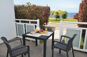 A balcony with a table set for breakfast, two chairs, and a view of the sea.