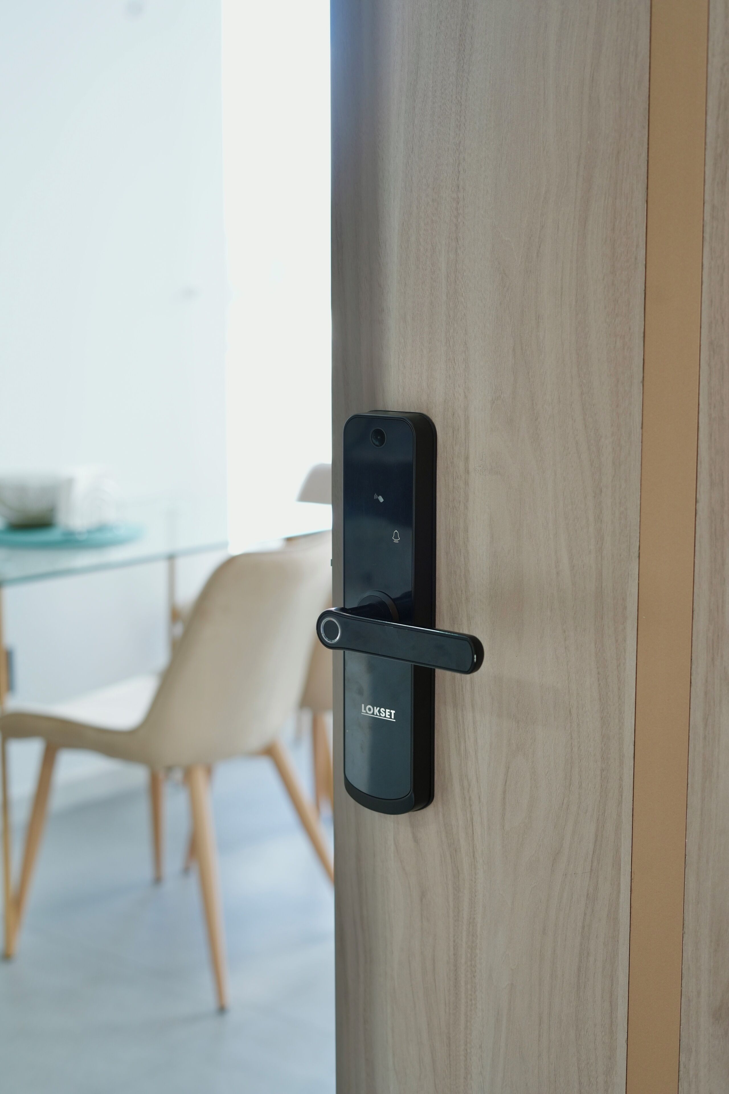 A modern door with a lockset, a glass table, and a chair in the background.