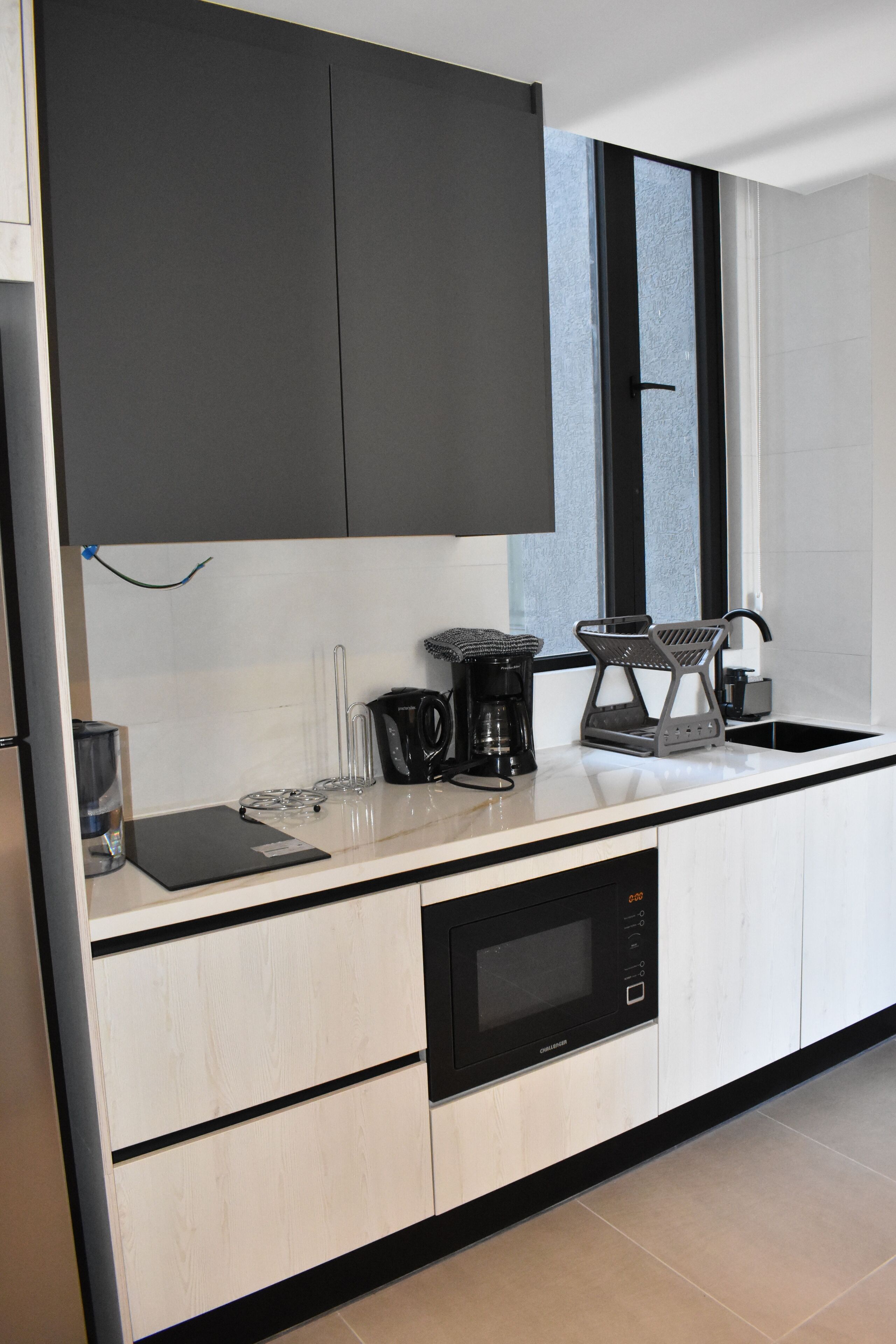 A modern kitchen with a built-in microwave, a coffee maker, and a kettle on the countertop.