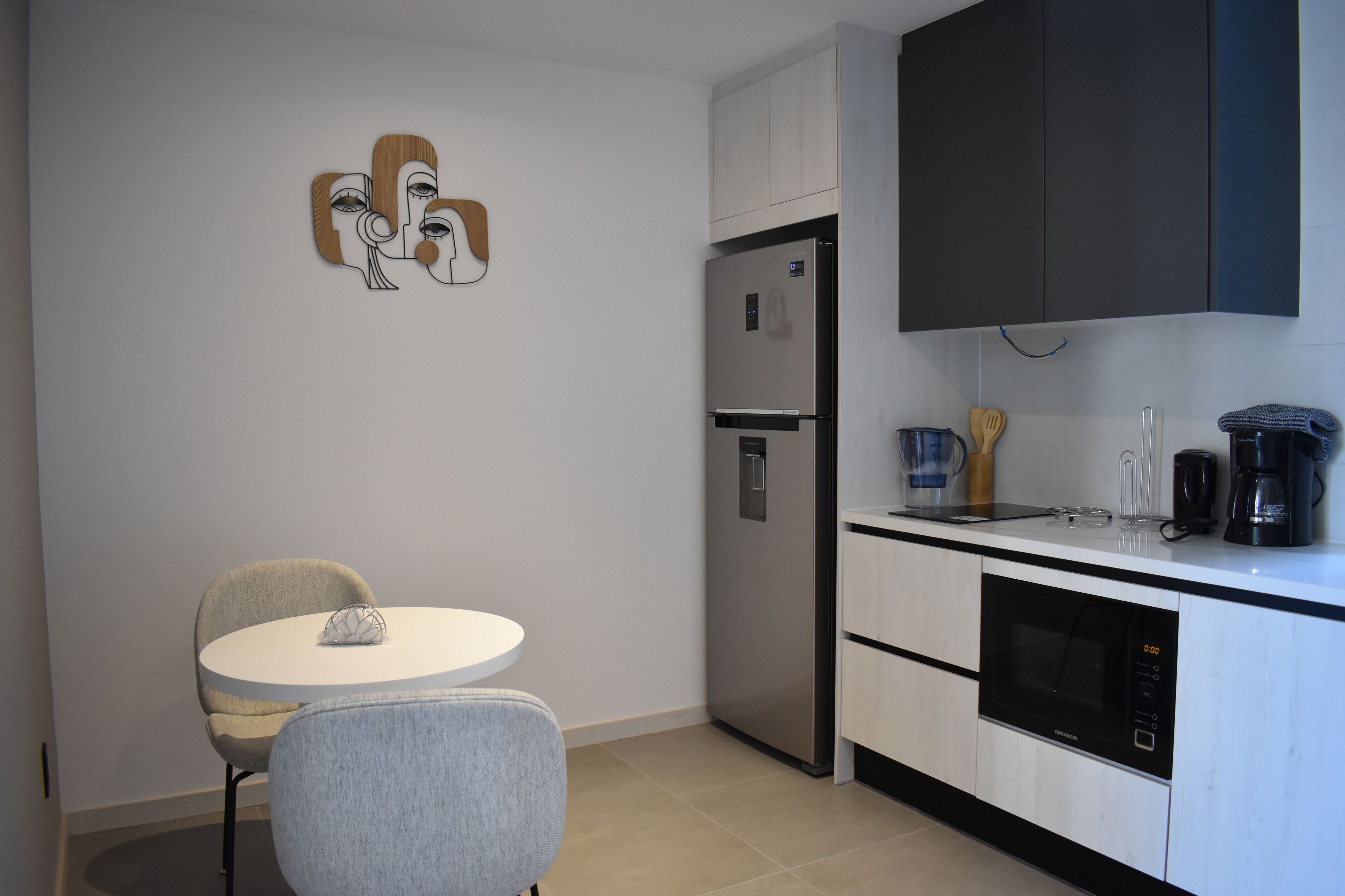 A modern kitchen with a built-in refrigerator, a microwave, and a coffee maker. There is a round dining table with two chairs.