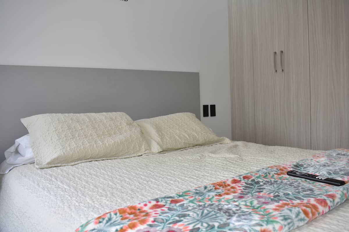 Una cama bien hecha con un edredón estampado con motivos florales y un control remoto encima.