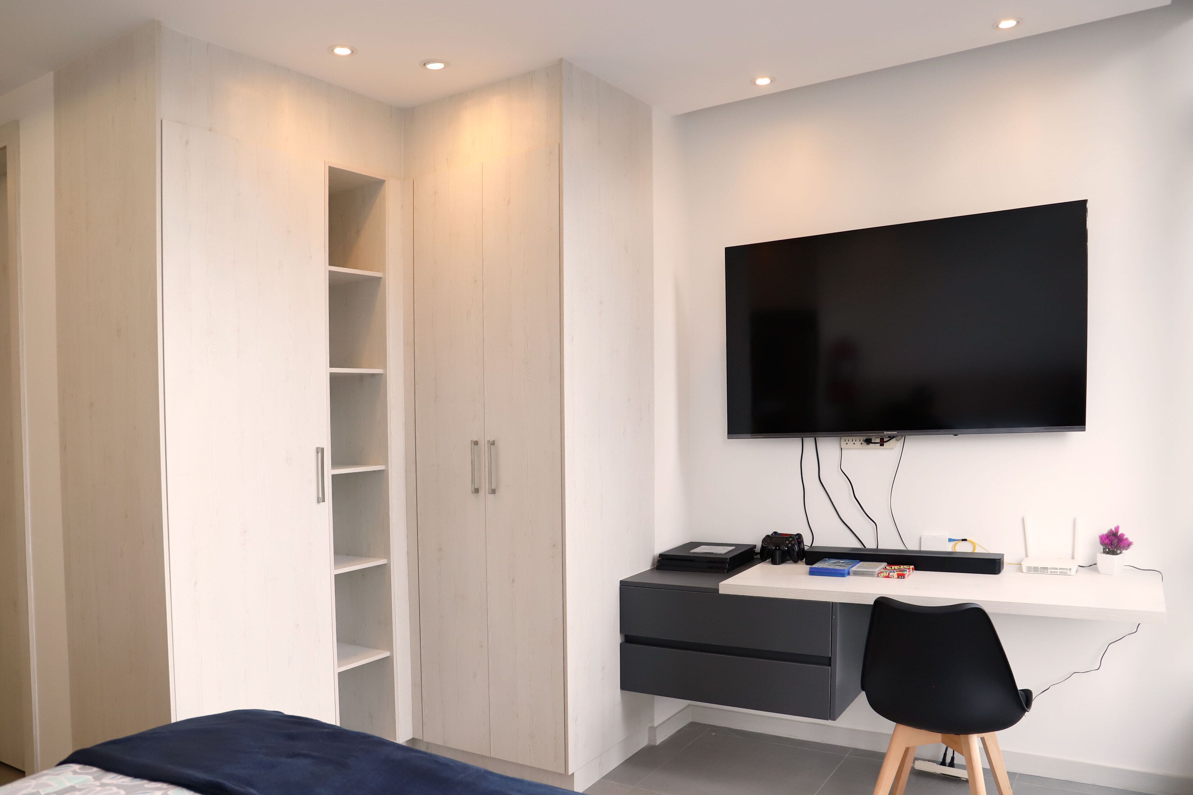 A bedroom with a bed, a wardrobe, a desk with a computer, and a TV.