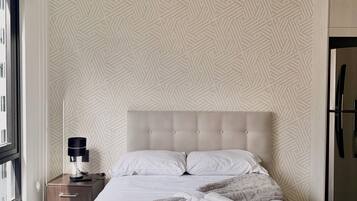 Ein ordentlich bezogenes Bett mit Kopfteil, ein Nachttisch mit Lampe und eine Wand mit Muster.