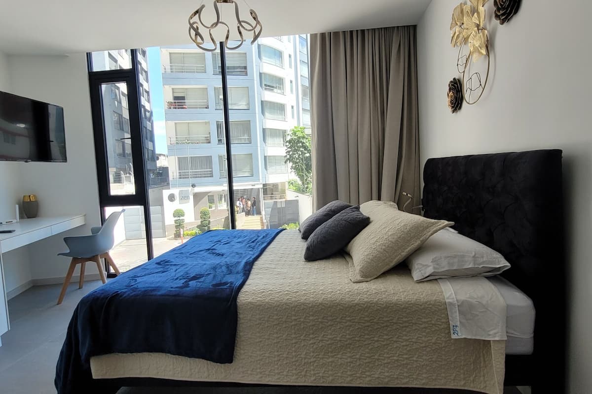 Un dormitorio moderno con cama, escritorio y ventana grande.